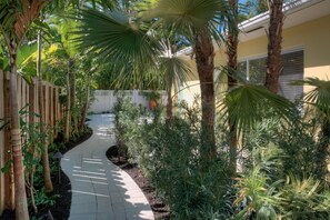 Stroll along the winding garden path, lined with lush tropical plants and a classic white picket fence.