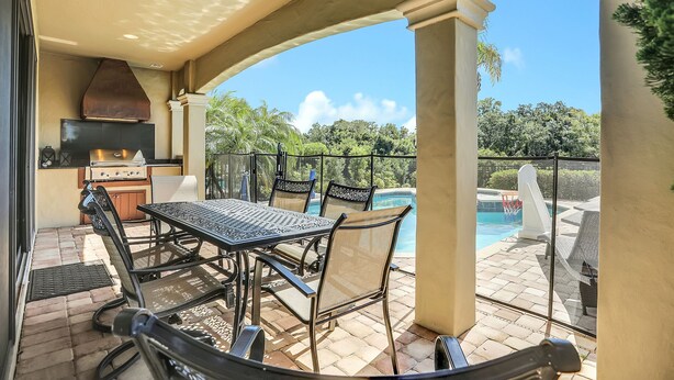 Un patio exterior con mesa y sillas, una parrilla y vistas a una piscina.