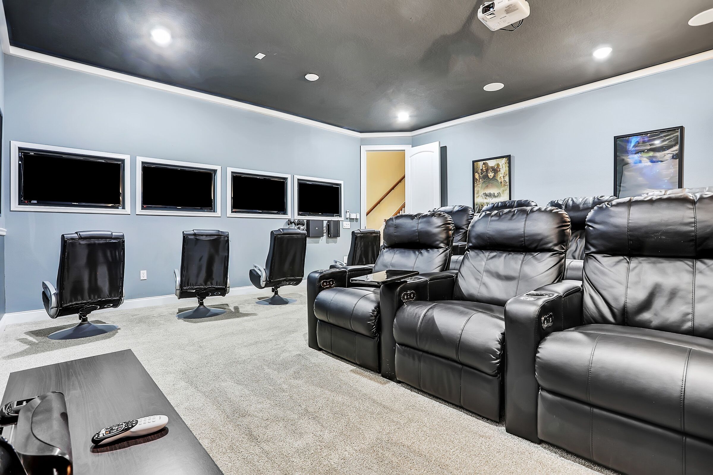 A home theater room with a reclining sectional sofa, a flat-screen TV, and a ceiling-mounted projector.