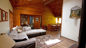 A cozy living room with a wooden ceiling, a sofa set, a dining table, and a fireplace.