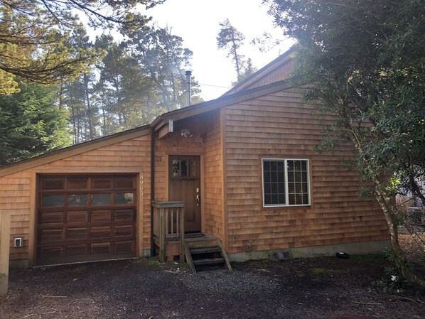 A single-story wooden house with a garage, a front door, and a small porch.