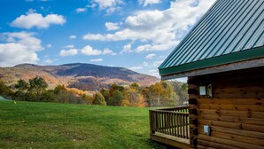 A wooden cabin with a green roof, a wooden deck, and a view of a mountain under a partly cloudy sky. - ✧Queen Cabin - wait until you see the BATHROOM! (Dryfork)