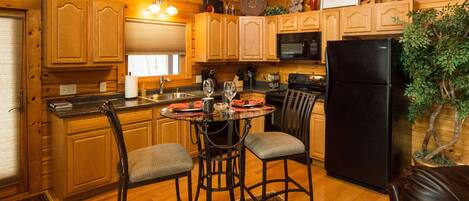 A wooden cabin-style kitchen with a dining table, chairs, and a refrigerator.