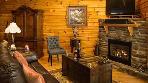 A cozy living room with a leather sofa, a coffee table, a fireplace, and a television mounted above it. - ✧Queen Cabin - wait until you see the BATHROOM! (Dryfork)