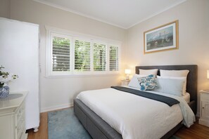 A bedroom with a bed, bedside tables, a nightstand, a window with blinds, and a painting on the wall. - Dogs Stay Free. Cosy Restful Retreat with Fireplace. (Wentworth Falls)