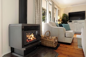 A modern living room with a wood-burning stove, a sofa, a television, and a wicker basket. - Camellia Cottage. Where Dogs Holiday Too. (Wentworth Falls)