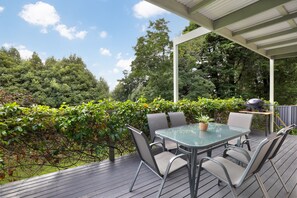 An outdoor patio with a glass table and chairs, surrounded by a wooden deck and a covered area.