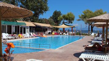 A poolside area with lounge chairs and umbrellas, a reception area, and a view of the sea.