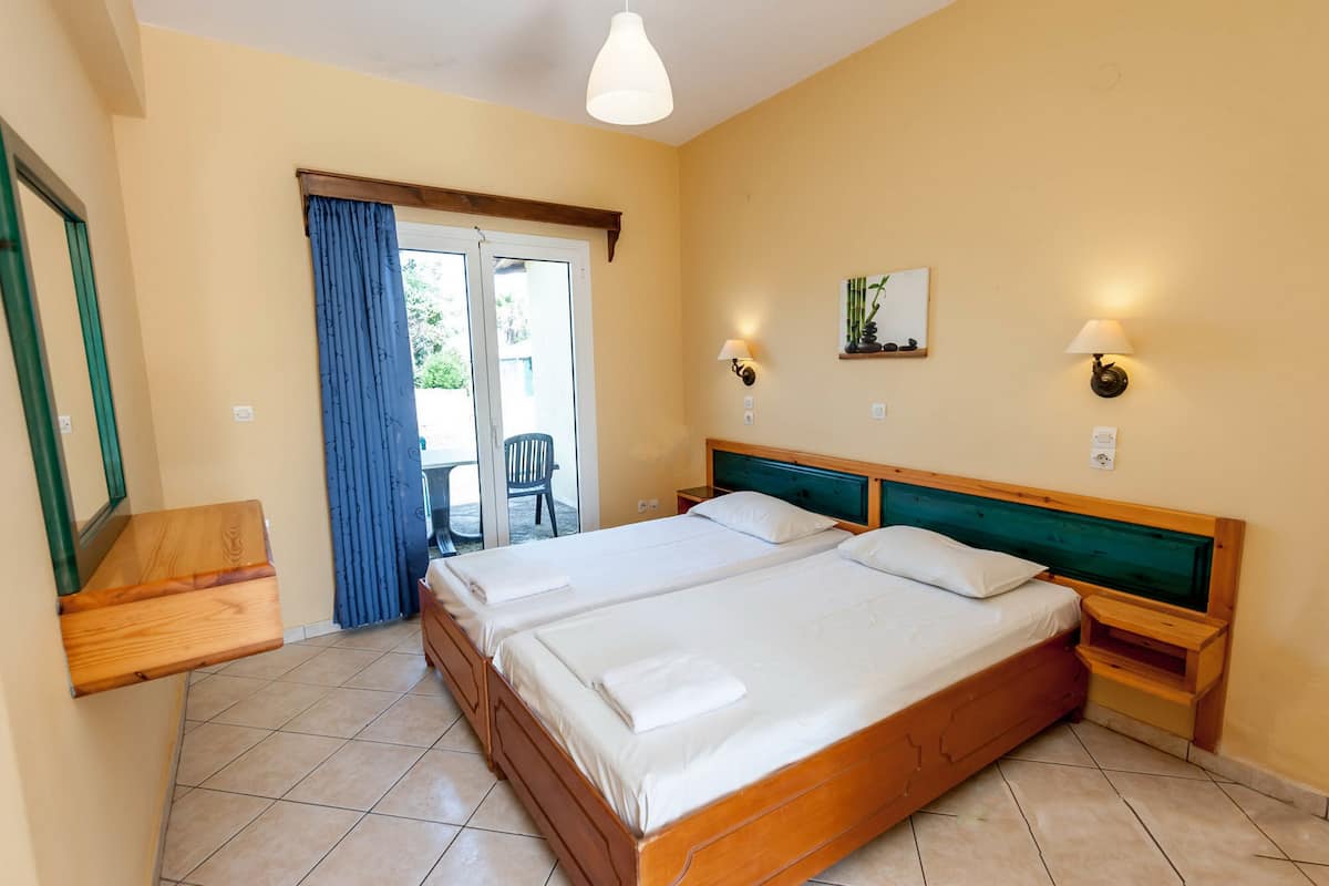 A hotel room with two beds, a wooden headboard, a small table, and a chair near the door.