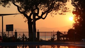 Un atardecer sobre una masa de agua tranquila, con un árbol en primer plano y una valla al fondo.