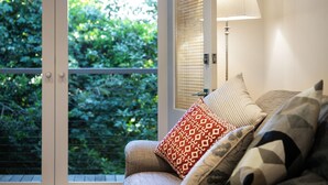 A room with a sofa, patterned cushions, a lamp, and a view of greenery through a window. - Haiku- charming oasis in Daylesford (Daylesford)