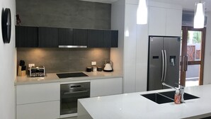 Uma cozinha moderna com armários escuros, geladeira de aço inoxidável, forno embutido e iluminação pendente.