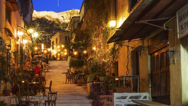 A narrow street with outdoor seating, potted plants, and string lights. - "Modern cozy renovated apartment is waiting for you in the heart of Athens.  (Athina)
