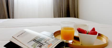 A neatly made bed with a tray containing a glass of orange juice, a cup, and a bowl of strawberries.
