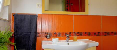 A bathroom with a white sink, orange and white tiles, a black towel, and a mirror above the sink.