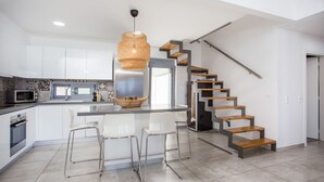 Una cocina moderna con armarios blancos, una isla central y una escalera con escalones de madera.