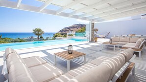 Un área de descanso al aire libre moderna con piscina, mobiliario blanco y vista al mar.
