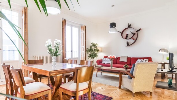 A spacious living area with a wooden dining table, chairs, a red sofa, and a coffee table.