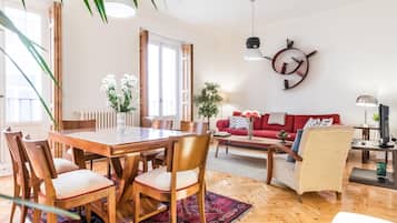 Een ruime woonkamer met een houten eettafel, stoelen, een rode bank en een salontafel.