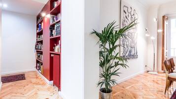 Ruime kamer met een visgraat parketvloer, een rode boekenkast vol boeken, een potplant en een lijst met abstracte kunst aan de muur.