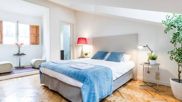 Een moderne slaapkamer met een groot bed, een nachtkastje met een lamp, een klein bijzettafeltje met een plant en een potplant bij het raam.