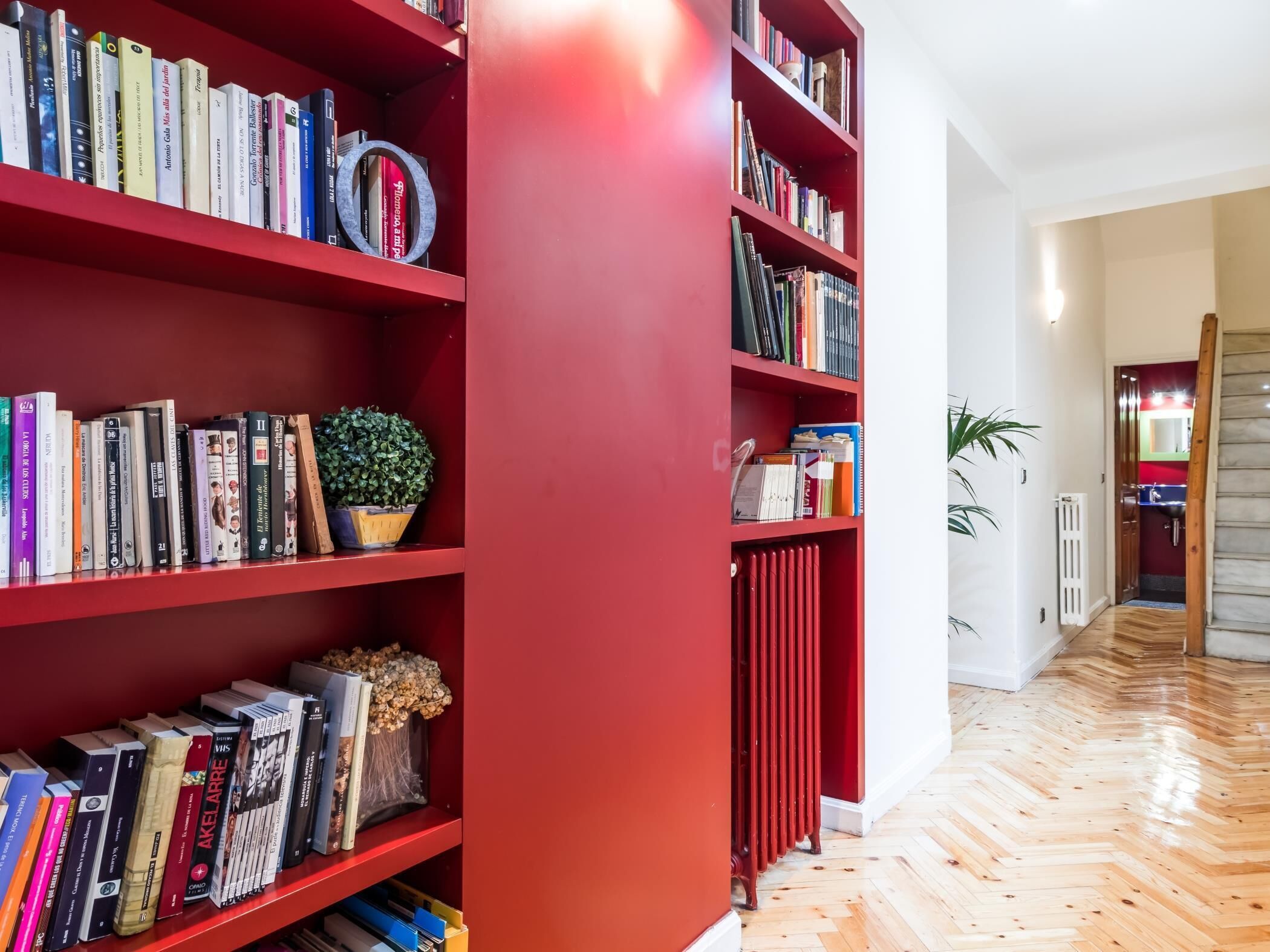 Une bibliothèque avec des étagères rouges remplies de livres et d’objets décoratifs.
