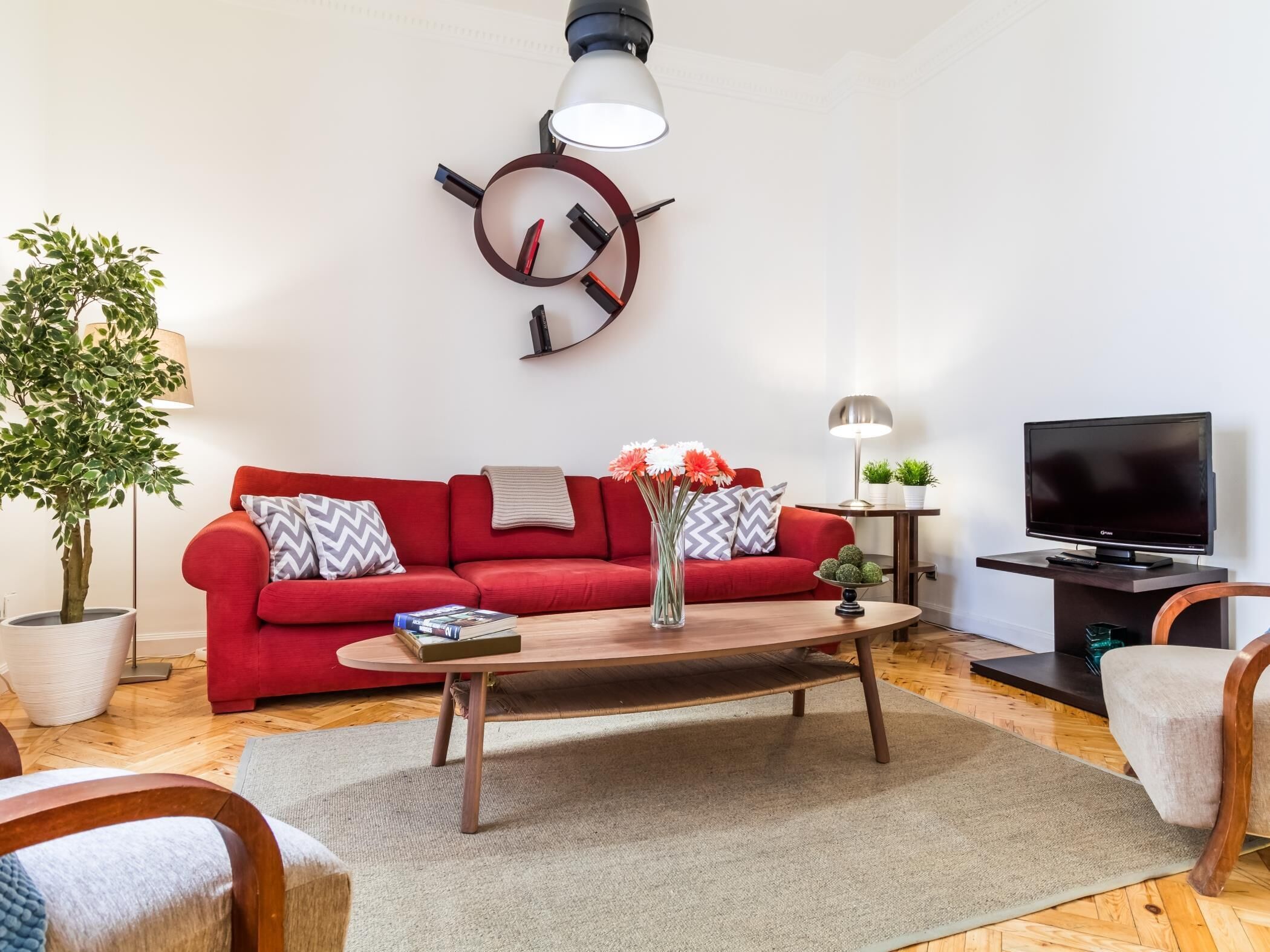 A modern living room with a red sofa, a coffee table, a TV, and a decorative wall piece.