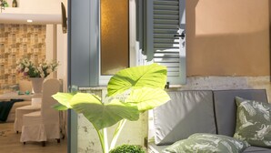 Uma sala de estar com sofá, uma planta verde grande e uma janela com persianas.
