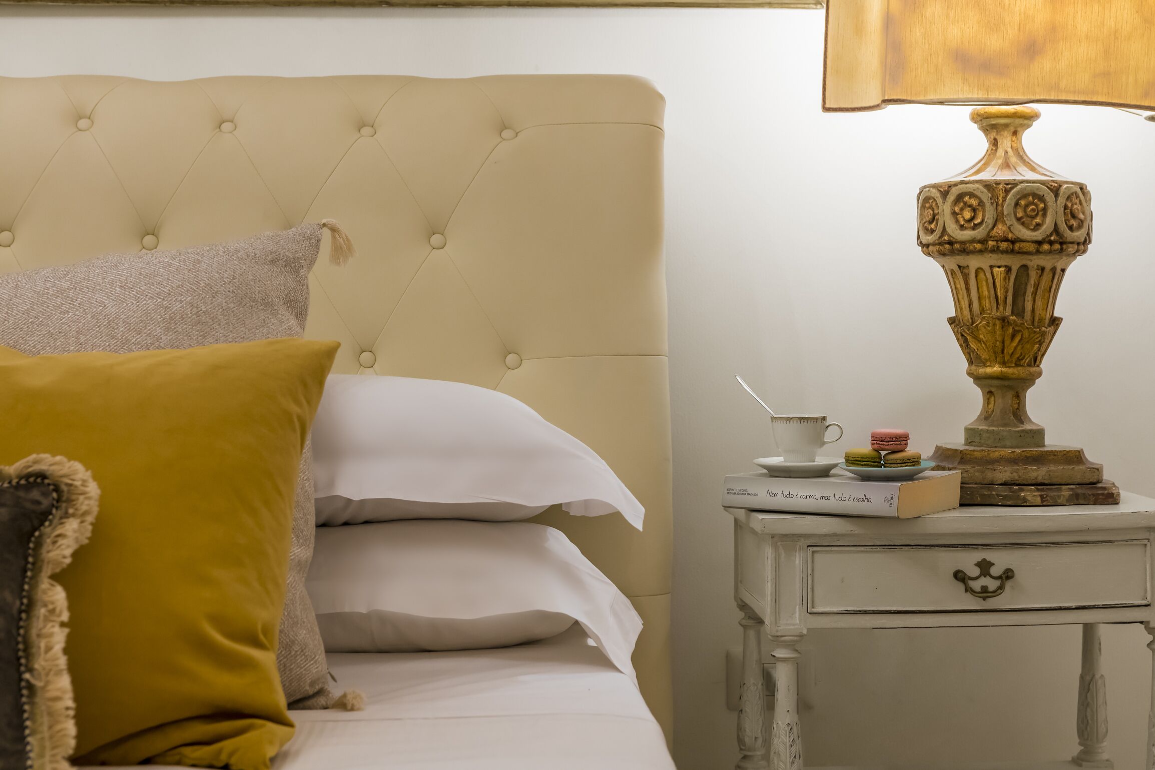 A bed with a tufted headboard, a bedside table with a lamp, and a book.