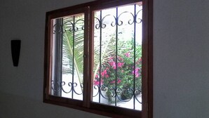 Een raam met decoratieve ijzeren spijlen en een houten omlijsting, uitkijkend op een tuin met roze bloemen en groene beplanting.