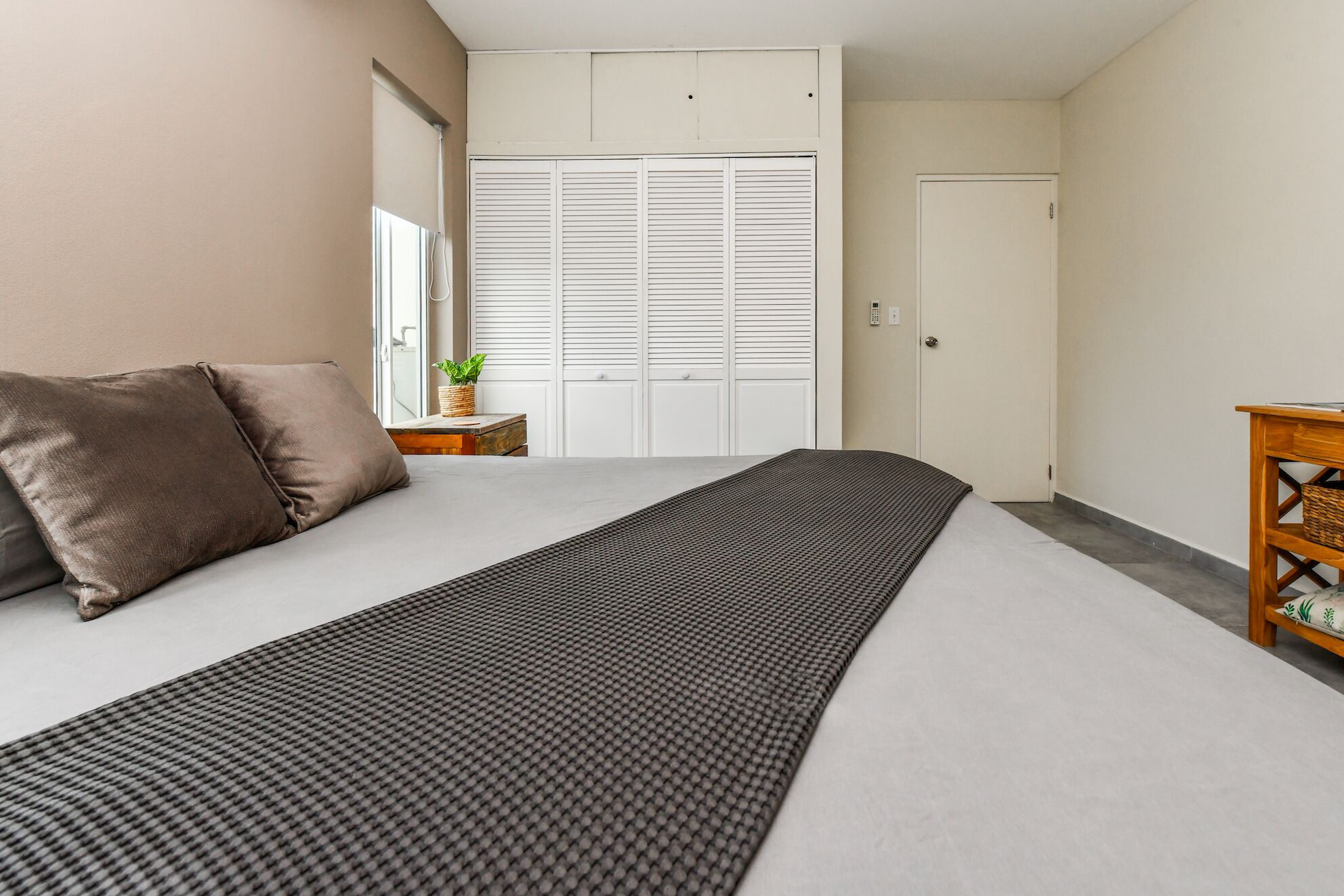 Une chambre à coucher comprenant un lit, une table de chevet, une petite table en bois, une plante en pot et une armoire avec des portes coulissantes.