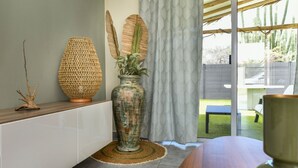 En modern inredning med en stor, vävd lampa, en rustik vas med växter och utsikt över en trädgård med ett trädäck och en kaktus.