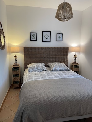 A neatly made bed with a patterned bedspread, two bedside lamps, a wicker headboard, and three framed pictures on the wall.