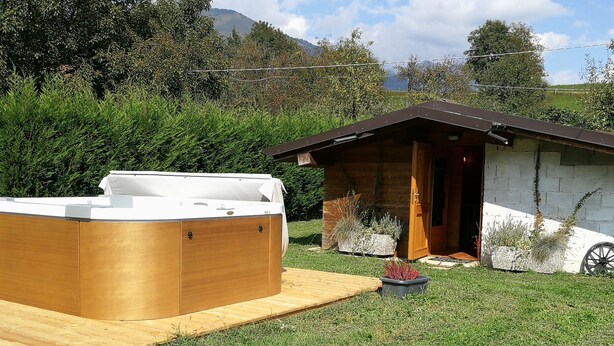 Un bain à remous en bois installé dans un jardin, avec une petite cabane en bois et une brouette.
