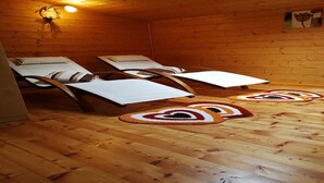 Une pièce aux murs et au sol en bois, deux fauteuils inclinables avec des coussins blancs, et un luminaire fixé au mur.