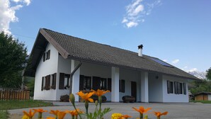 Une maison blanche avec un toit en pente et une cheminée, entourée de fleurs et sous un ciel dégagé.
