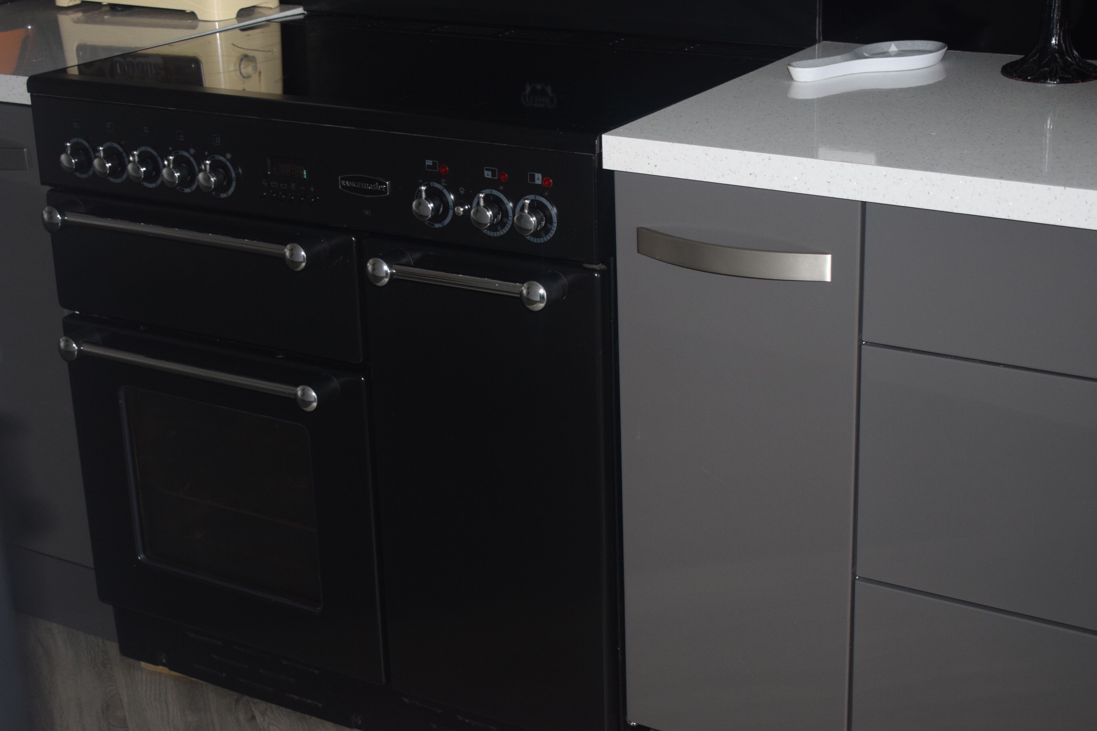 Uma cozinha com fogão preto, bancada branca e forno de aço inoxidável.