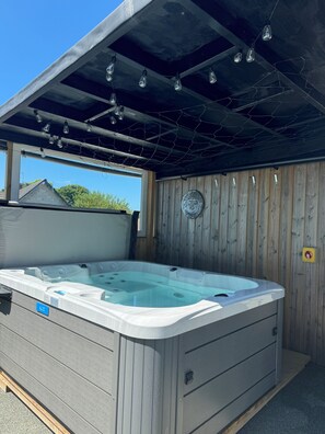 A hot tub with a wooden deck and a metal roof, surrounded by a wooden fence.