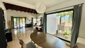 A spacious living area with a large sliding glass door leading to a patio, a round wooden table, and a modern ceiling light. - Aloe Villa - Spacious and luminous villa with heated pool -Fiber (La Oliva)