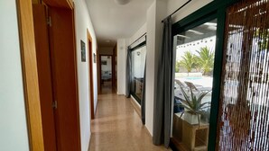 A hallway with wooden doors, a tiled floor, and a view of a pool area with lounge chairs and a plant. - Aloe Villa - Spacious and luminous villa with heated pool -Fiber (La Oliva)