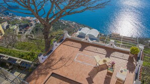 Una terraza en la azotea con vista al mar, un árbol y suelo de baldosas.