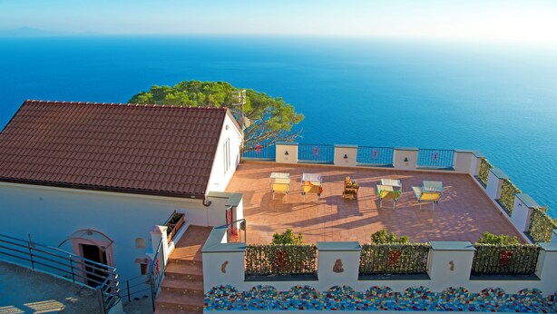 Una terraza en la azotea con mobiliario exterior, vistas al mar y un edificio con techo de tejas.