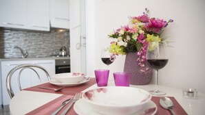 Una mesa de comedor con platos, cubiertos, copas de vidrio rosa, un florero con flores y dos copas de vino.