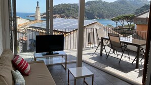 A balcony with a TV, seating, and a view of the sea and hills. - Beautiful Apartment with Sea Views and the Port of Fornells (Fornells)