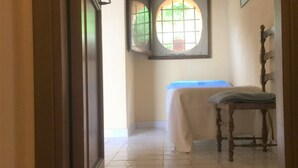 A hallway with a tiled floor, a window with bars, a chair, and a table with a blue cloth. - Bed & Breakfast Baglio Fanara # 2 (Suite) (San Vito lo Capo)