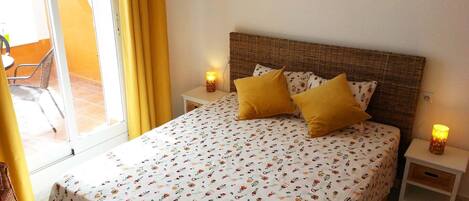 A bedroom with a large bed, two bedside tables, a wicker headboard, and a view of the outside through a glass door.