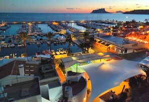 Un port de plaisance au crépuscule, avec des bateaux amarrés, un espace de repos abrité et des bâtiments dotés de balcons.