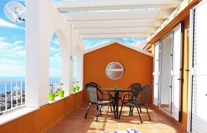 Un balcon avec une table et des chaises, une vue sur la mer et un mur blanc avec une fenêtre.