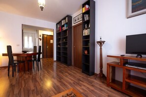 A living room with a wooden floor, a dining table with chairs, a bookshelf, a television, and a lamp. - Rialto Apartment Vatican Museums (Rome)
