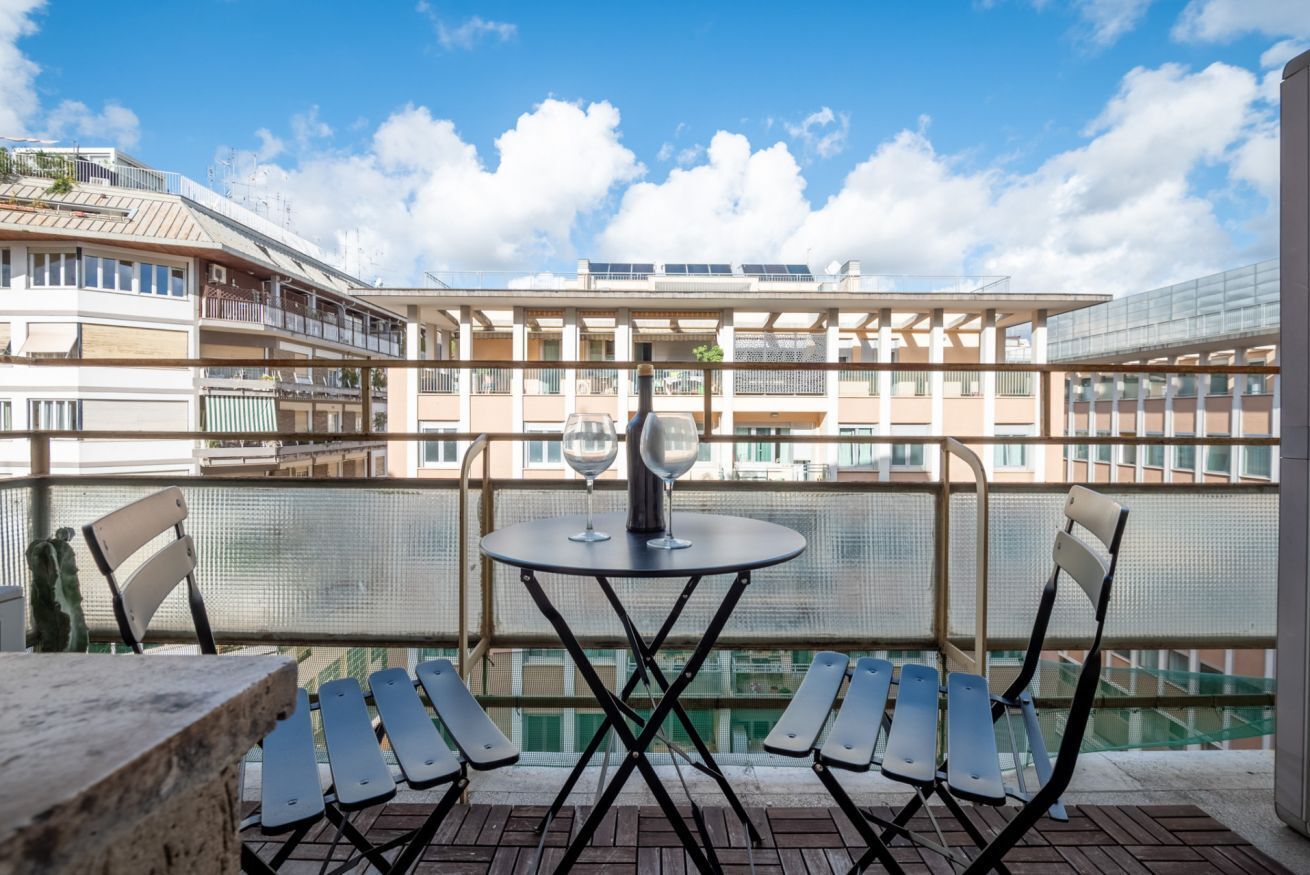 Un balcon avec une table et des chaises, une bouteille de vin et une vue sur un immeuble doté de balcons et de fenêtres.